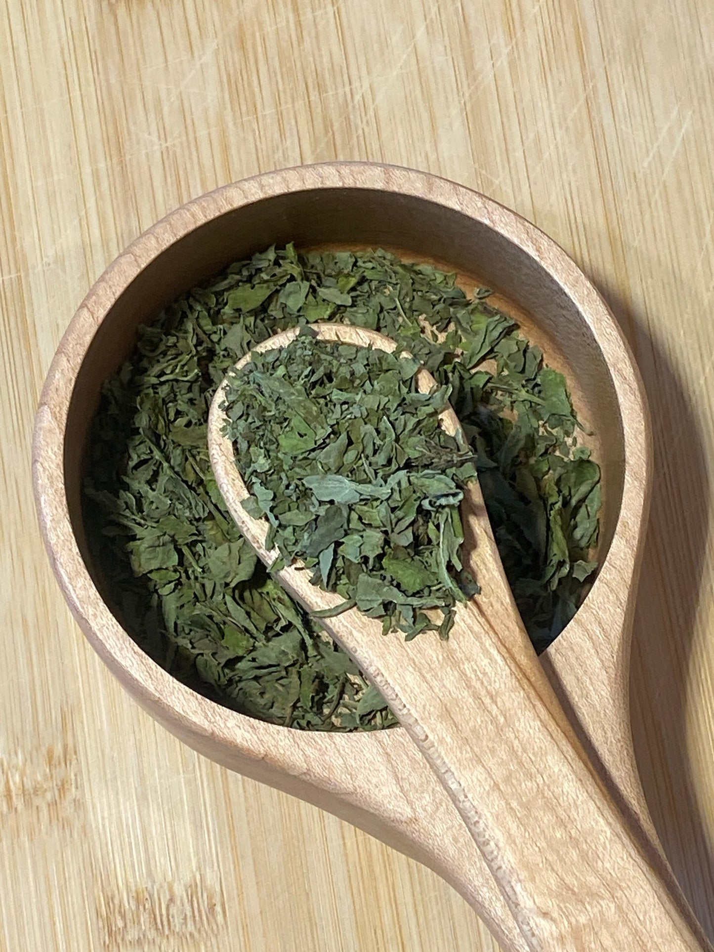 Premium dried basil leaves grown in Texas shown in a spoon and bowl for culinary flavors and cooking.