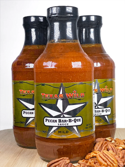 Three bottles of Texas Wild® Pecan Bar-B-Que Sauce on a wooden surface with pecans. Available at TexasWildBrand.com